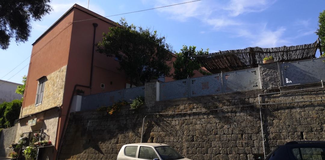The rustic stone-walled exterior of the property with a terracotta-toned building and parked car, showing the characteristic Mediterranean architecture.